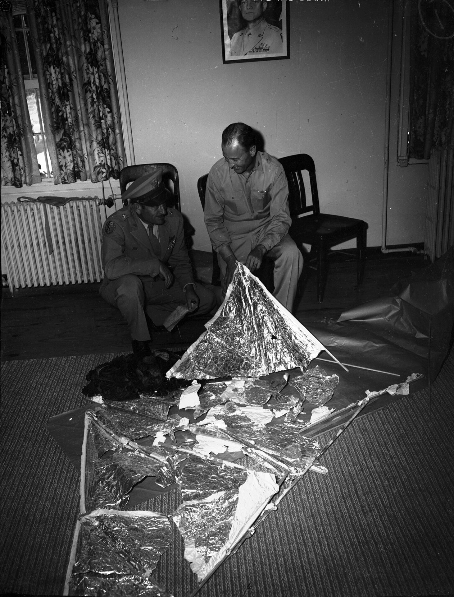 General Roger Ramey and Colonel Thomas DuBose examining recovered weather balloon debris on the floor, Fort Worth Army Air Field, July 8, 1947 (public domain)